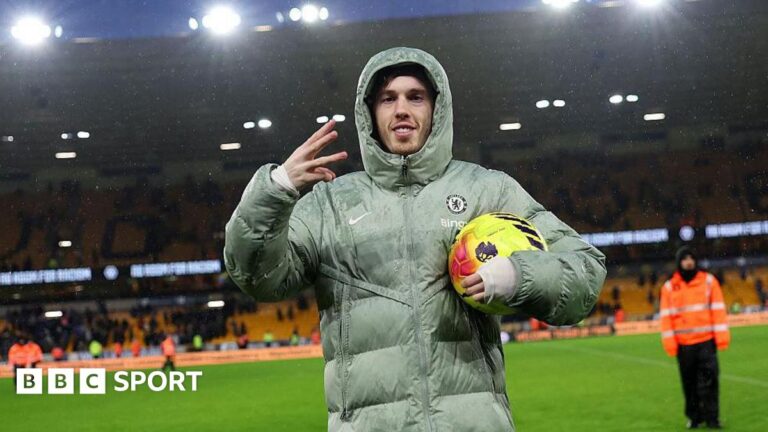 Cole Palmer: Is Chelsea forward in World Cup picture for England after hat-trick at Wolves? Cole Palmer celebrates scoring a hat-trick for Chelsea with a three-finger salute with his right hand, while holding the yellow match ball under his left arm and wearing a large Chelsea puffer jacket with the hood up.